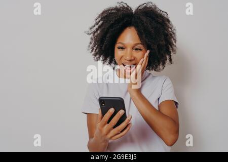 Une jeune femme afro-américaine joyeuse reçoit de super nouvelles sur smartphone Banque D'Images