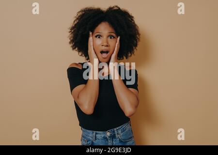 Photo d'une femme aux cheveux bouclés, à la peau sombre, qui tient les mains sur les pommettes Banque D'Images