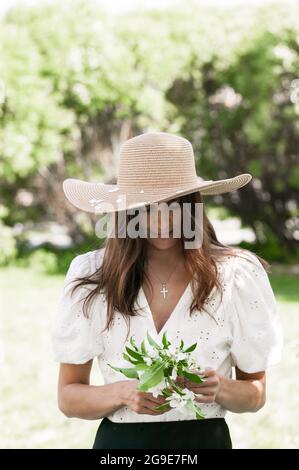 Jolie et jeune belle jeune femme de race blanche. Une femme attrayante et souriante tient une fleur de pomme. Mignon et beau brunette modèle i Banque D'Images