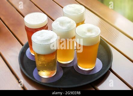 Cinq bières froides avec des têtes de mousse dans des verres sur un plateau sur une table extérieure en lamelles dans une vue de gros plan en grand angle Banque D'Images