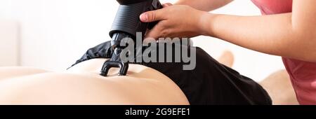 Arrière-plan du pistolet de massage. Une jeune physiothérapeute féminine utilise un appareil de massage portatif pour soulager les douleurs dans le bas du dos pendant la séance de physiothérapie. Web bann Banque D'Images