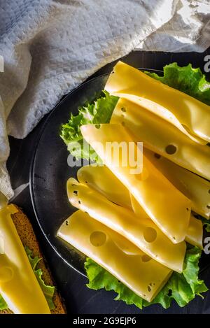 fromage dur avec de grands trous tranchés sur une assiette avec des feuilles de laitue Banque D'Images