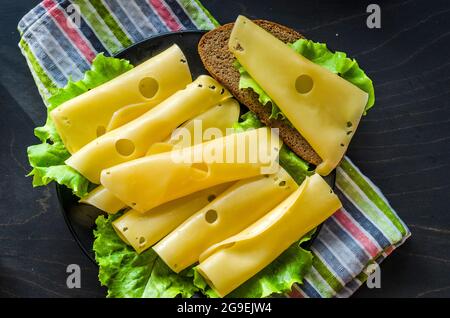 fromage dur avec de grands trous tranchés sur une assiette avec des feuilles de laitue Banque D'Images