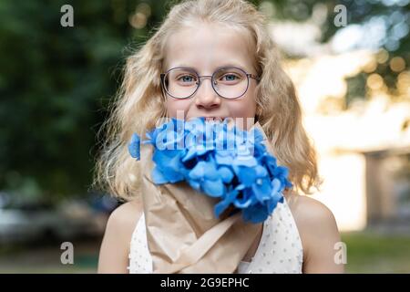 Petit mignon adorable blond caucasien petite femme fille portrait tenir beau bleu frais hortensia bouquet à l'extérieur de la ville parc jardin sur chaud Banque D'Images