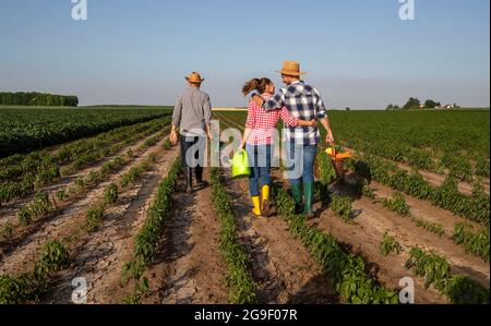 Un jeune homme et une jeune femme revenant de travailler dans le champ portant le panier avec des légumes et arrosoir peut embrasser. Éleveur principal transportant la houe de jardinage wal Banque D'Images