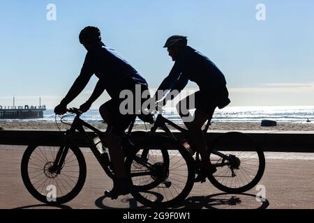 Faire du vélo deux cavaliers sur des vélos silhouetted non reconnaissable promenade du front de mer avec les vagues de fond . Banque D'Images