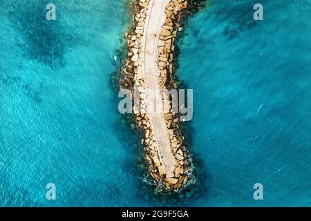 Vue aérienne en haut vers le bas du brise-lames en pierre sur la surface bleu vif de la mer. Banque D'Images