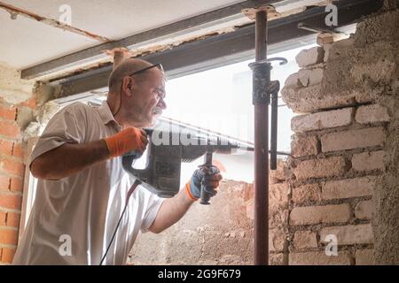 Ouvrier de construction avec marteau de démolition cassant un mur intérieur. Banque D'Images