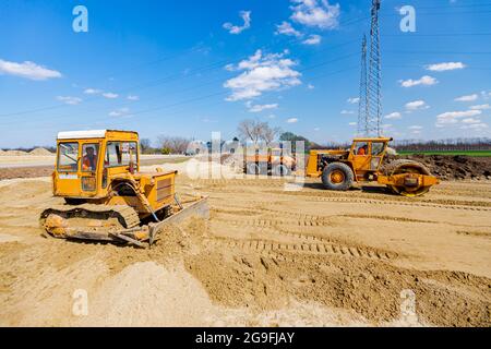 Le rouleau de route avec pointes, le bulldozer et le camion avec compacteur de vibrations à plaque monté sont compactés, nivelant le sable pour les fondations de la route sur le chantier Banque D'Images