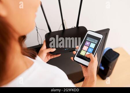 Mains d'une femme connectant l'application Smart Home de son téléphone au routeur wi-fi Banque D'Images