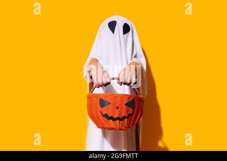 Enfant en costume fantôme tenant un panier en forme de citrouille devant lui. Banque D'Images