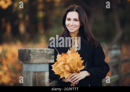 Photo d'une femme attrayante va pour une promenade dans le parc d'automne et tient un bouqet de feuilles jaunes Banque D'Images