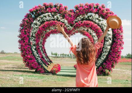 jeune femme en robe rose et le chapeau se tient et lever ses mains sur fond de fleur coeur arches amour. Image avec un foyer sélectif sur la fille. Cœur Banque D'Images