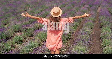 Jeune belle femme avec robe rose et chapeau appréciant la liberté de beauté et le parfum d'un champ de lavande en fleur panoramique bannière Banque D'Images