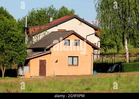 Petite maison familiale suburbaine avec dessus recouvert de nylon noir deux fenêtres et portes en bois délabrées sur hangar attaché à côté de plus grande maison blanche Banque D'Images