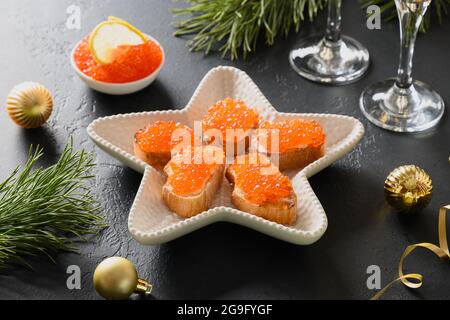 Canapés russes avec caviar rouge sur ciabatta sur fond noir pour Noël, fête du nouvel an. Repas de fête. Gros plan. Banque D'Images