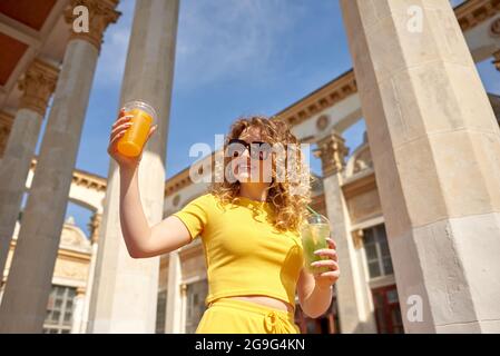 jolie fille en costume jaune d'été avec limonade dans ses mains dans le centre historique Banque D'Images