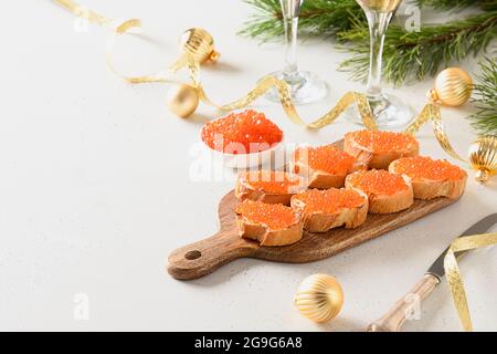 Canape avec caviar rouge servi sur une planche à découper en bois sur fond blanc pour Noël, fête des fêtes du nouvel an. Repas de fête. Gros plan. Copier l'espace. Banque D'Images