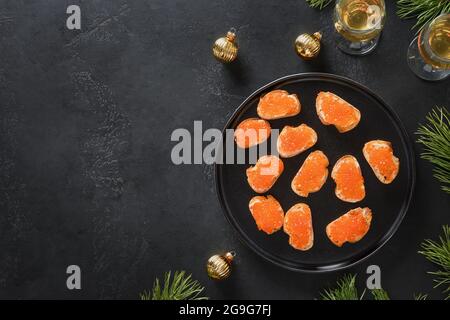 Canapés russes avec caviar rouge sur ciabatta sur fond noir pour Noël, fête du nouvel an. Repas de fête. Gros plan. Banque D'Images