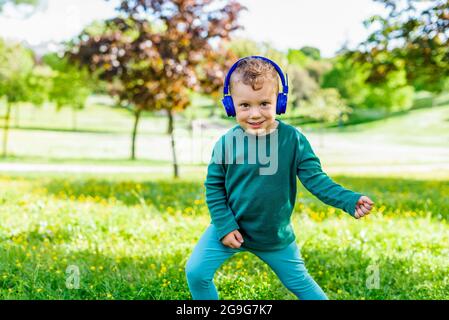 un jeune enfant heureux qui écoute de la musique en plein air dans un parc. un petit enfant souriant qui danse en plein air dans un jardin, qui porte des écouteurs et fait de la fausse guitare jouer Banque D'Images