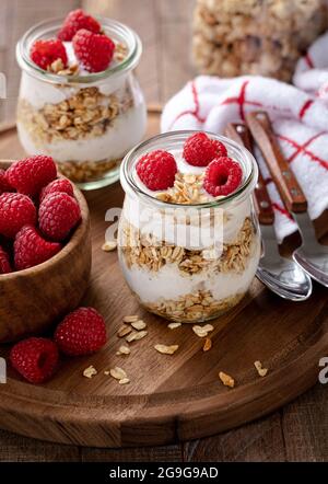 Fait de granola avec yaourt et framboises fraîches sur un plateau en bois Banque D'Images