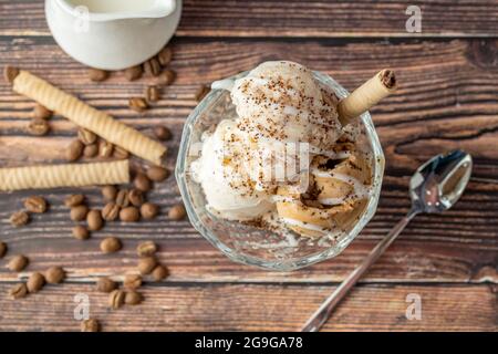 Glace Roma au noyer, à la crème et au caramel dans un bol en verre avec du café moulu et de la sauce au chocolat blanc. Banque D'Images