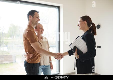 Vue latérale portrait d'un jeune couple qui se secoue la main avec un agent immobilier pendant la visite de l'appartement, espace copie Banque D'Images