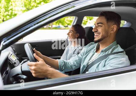 Homme et femme joyeux du Moyen-Orient assis dans une belle voiture, regardant la route et souriant, ayant la conversation, discutant de leur voyage, amoureux multiraciaux Banque D'Images