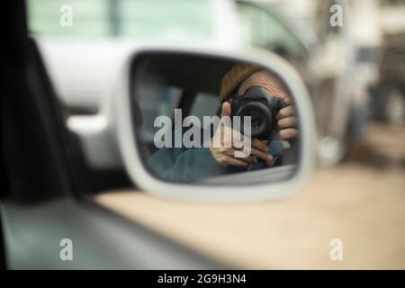 Le photographe prend des photos de lui-même dans le miroir. Utilisation de la caméra dans la voiture. Regarder à travers la lentille du rétroviseur. Autoportrait Banque D'Images