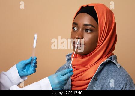 Femme noire dans le hijab faisant le test nasal par écouvillon sur fond de studio, infirmière ou médecin méconnaissable avec des écouvillons de coton prenant le test pcr pour l'amérique africaine Banque D'Images