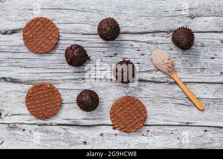 Vu d'en haut, sur des planches en bois sont de petits gâteaux au chocolat, des biscuits au chocolat et une cuillère en bois avec de la poudre de chocolat. Banque D'Images