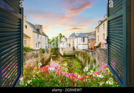 Vue par une fenêtre ouverte avec des volets au-dessus d'un petit ruisseau avec des maisons médiévales à proximité, au coucher du soleil dans le village français de Bayeux, en France, dans le N Banque D'Images