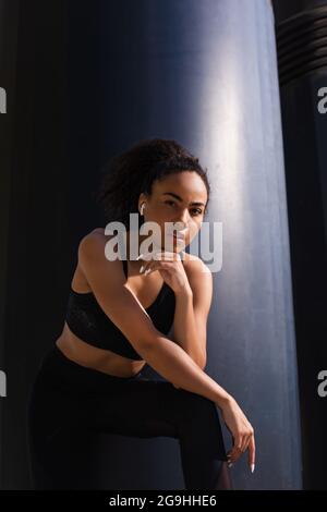 African american sportswoman dans les écouteurs regardant la caméra à l'extérieur pendant la journée Banque D'Images