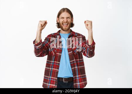 Oui gagnant. Heureux heureux homme blond se réjouissant gagner, criant de joie, de chanter et de célébrer, en secouant les mains levées joyeuse, atteindre le but Banque D'Images