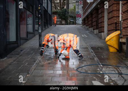 Bristol, Royaume-Uni. 22 mars 2021. Le matin après que Bristol ait été témoin de sa pire violence dans la rue pendant plusieurs années, le processus de nettoyage commence par le nettoyage des graffitis et le balayage des débris. Des manifestants ont attaqué hier la police après que des milliers de personnes aient assisté à une manifestation selon laquelle les officiers avaient « fortement conseillé » de ne pas se joindre à eux. Les policiers ont subi des fractures et les véhicules de police ont été mis à feu alors que des scènes de colère se déroulaient dans le centre-ville de Bristol. Photo : les nettoyeurs brossent les graffiti sur la chaussée à St Johns Steep, au centre de Bristol. Banque D'Images