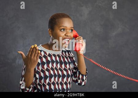 Jeune femme à la peau sombre avec un combiné rétro à fil rouge a une conversation intéressante. Banque D'Images