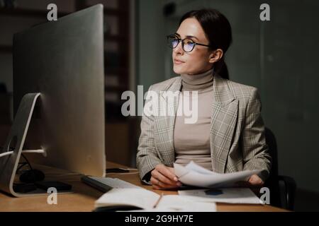 Femme charmante et concentrée travaillant avec un ordinateur et des papiers au bureau Banque D'Images