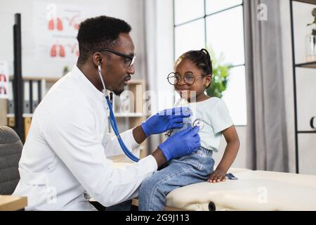 Concept de pédiatrie et de vérification régulière. Agréable soin Afro-American homme médecin vérifiant littel Afrique kid girl battement de coeur et souffle en utilisant le stéthoscope, travaillant dans le centre médical Banque D'Images