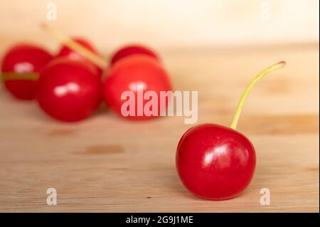 Une cerise rouge isolée avec un groupe de cerises en arrière-plan, sur une table en bois Banque D'Images