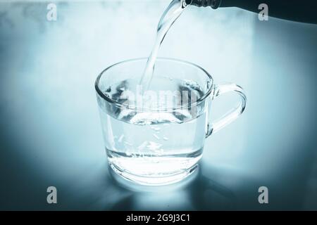 Verser de l'eau dans un fond bleu pastel en verre Banque D'Images