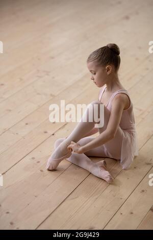 Portrait de la petite ballerine fille regardant l'appareil-photo tout en étant assis sur le plancher de bois dans la discothèque Banque D'Images