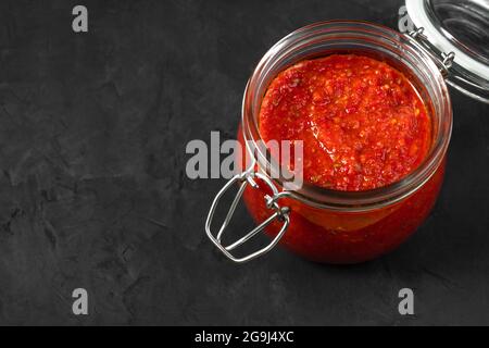Sauce Harissa. Adjika. Sauce au piment fort dans un pot sur fond noir. Tunisie, cuisine géorgienne et arabe. Copier l'espace. Banque D'Images