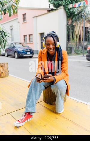 Italie, Milan, femme souriante avec casque et smartphone en ville Banque D'Images