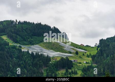 Parc solaire, centrale photovoltaïque située sur une pente de montagne dans les Alpes. Journée brumeuse, herbe de pâturage verte et ciel bleu et montagnes créent un f Banque D'Images