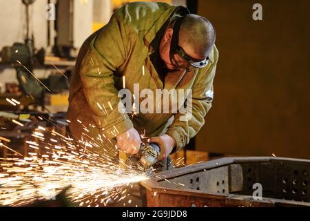 Gros plan de l'employé utilisant une meuleuse pour meuler le métal dans le usine Banque D'Images