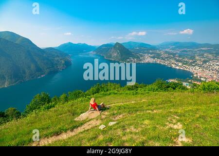 Femme assise au sommet de la ville suisse de Lugano, près du lac de Lugano en Suisse. Vue aérienne depuis le mont Monte Bre. Paysage urbain de Lugano avec San Salvatore Banque D'Images