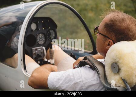 Pilote de planeur mature dans l'avion avant le vol. Regardant le panneau de commande ou l'avion sur le terrain. Avion à voilure fixe sans moteur. Un sport de haut niveau Banque D'Images