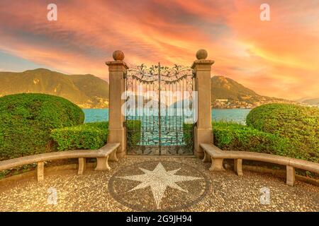 Porte sur le lac de Lugano dans le parc public de Ciani en Suisse. Coucher de soleil rouge au bord du lac de la ville de Lugano dans le canton du Tessin. Garez le banc avec le vent Banque D'Images
