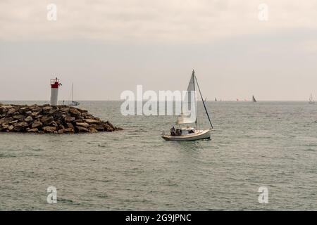 Mississauga, Ontario, Canada - juillet 4 2021 : un voilier avec trois personnes à bord, naviguant sur le lac Ontario, en passant par le phare de la promenade Lakefront Pa Banque D'Images