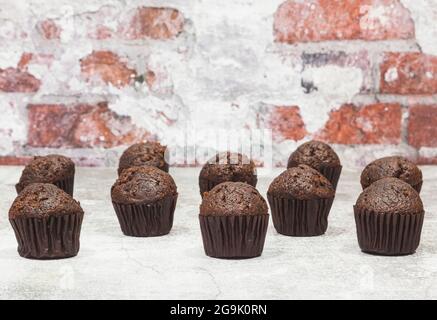 Sur une surface grise en face d'un mur de briques sont placés de nombreux cupcakes au chocolat. Banque D'Images